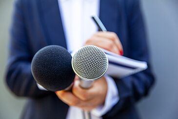 Female journalist at news conference or media event, writing notes, holding microphone