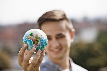 ein kleiner Globus wird von einer männlichen Person in der rechten Hand hochgehalten