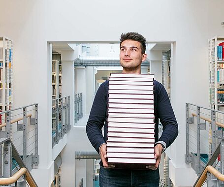 Studierender trägt Bücher in der Bibliothek